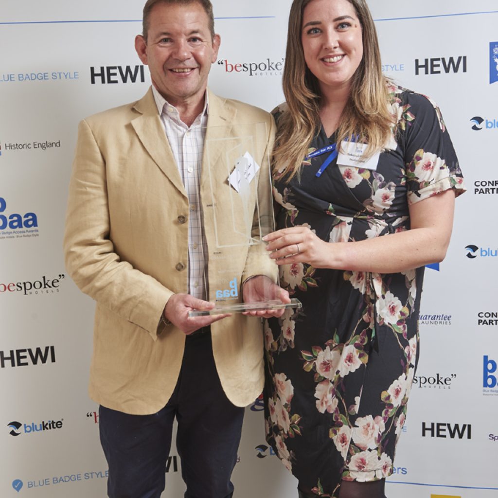 man in yellow jacket receiving glass award from woman in white flowers on black dress