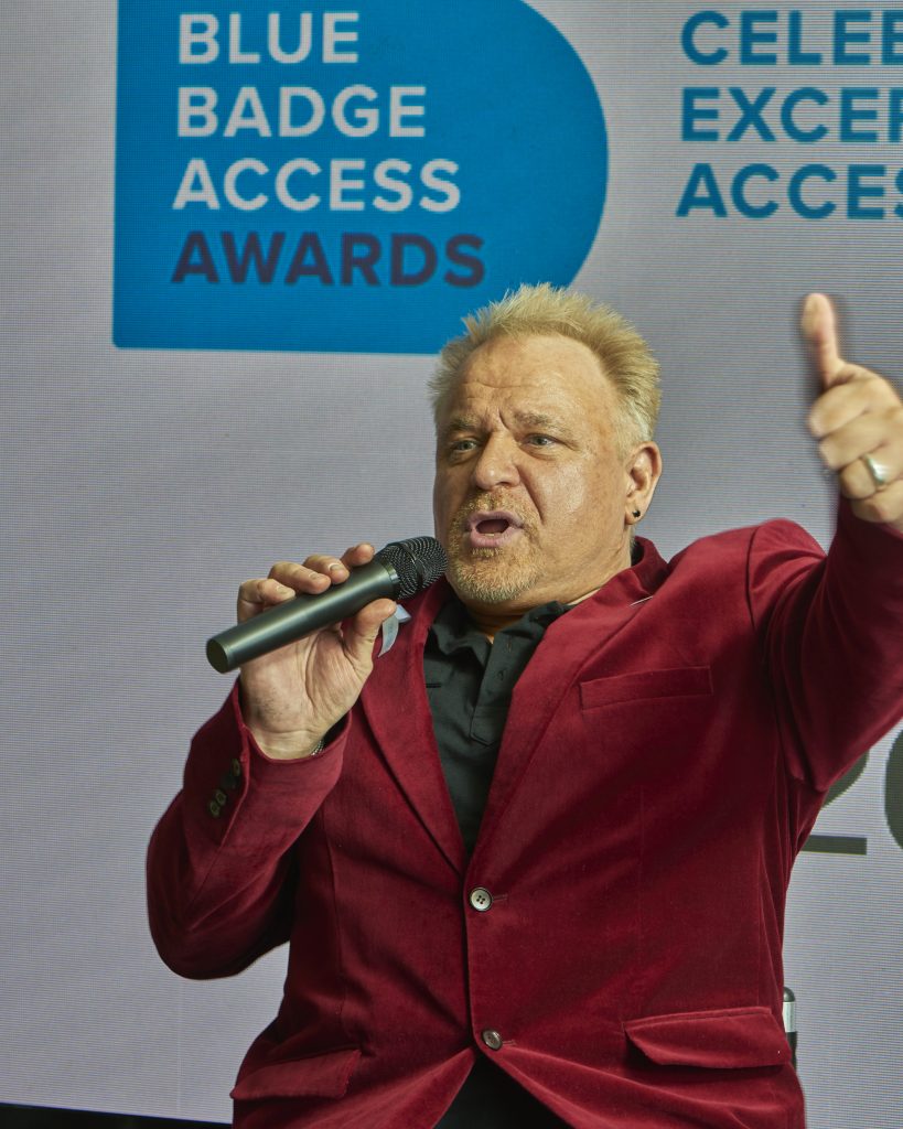 blonde haired man with microphone wearing red jacket